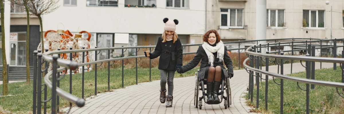 Woman in a wheelchair walking outdoors with a child on an accessible pathway