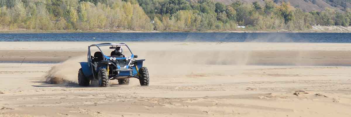 A blue tractor driving along the sandy beach, with a body of water visible in the background