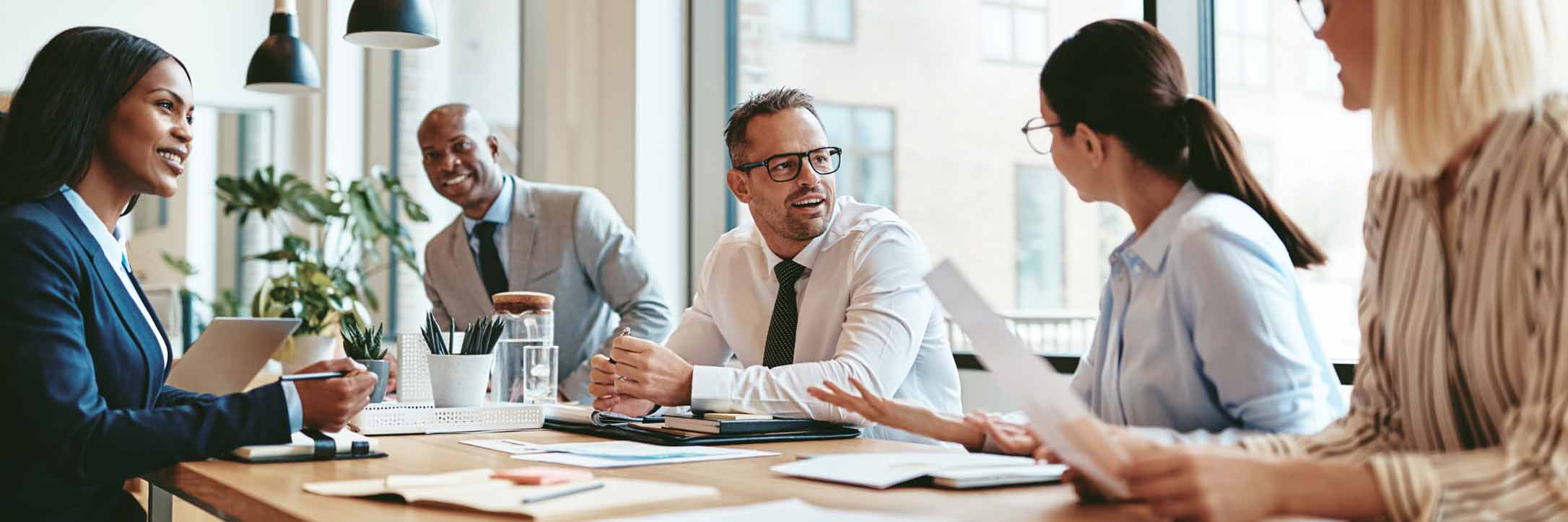 A diverse group of business professionals engaged in discussion around a conference table.<br />
